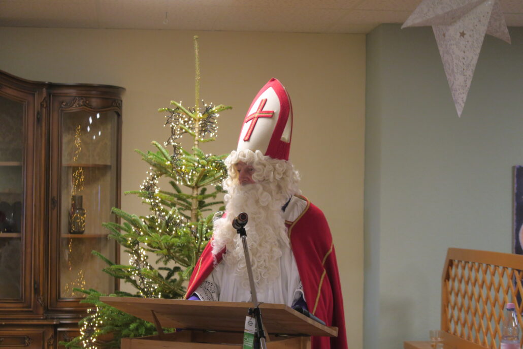 Ein Mann ist als Nikolaus verkleidet und steht an einem Rednerpult. Vor ihm ein Mikrofon.