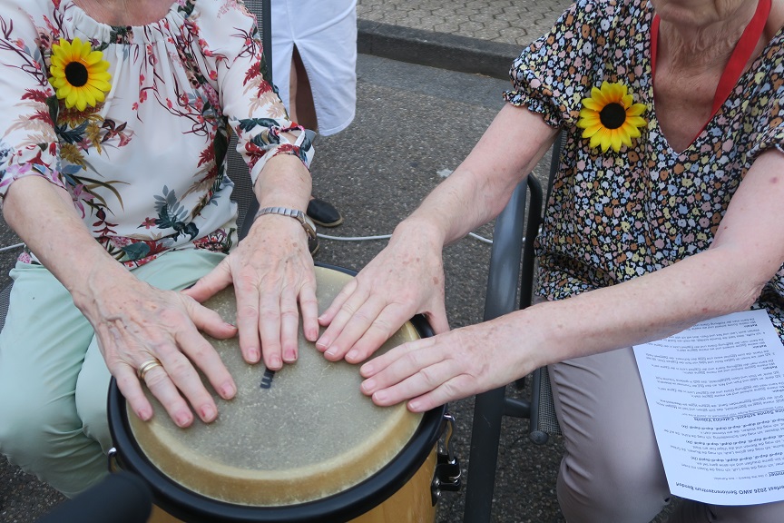 Die Hände von zwei Senior*innen berühren eine Trommel.